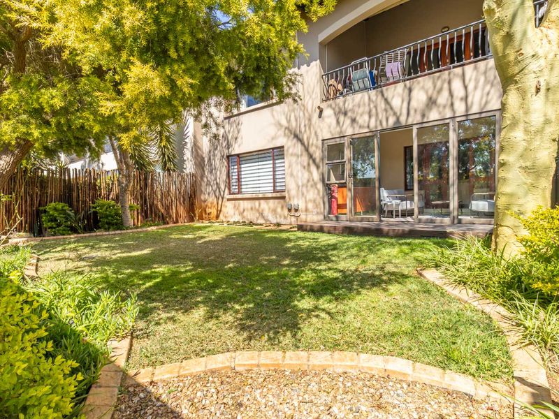Rear view of the townhouse featuring a private garden, wooden decking, sliding glass doors, and an upper-level balcony with metal railings.
