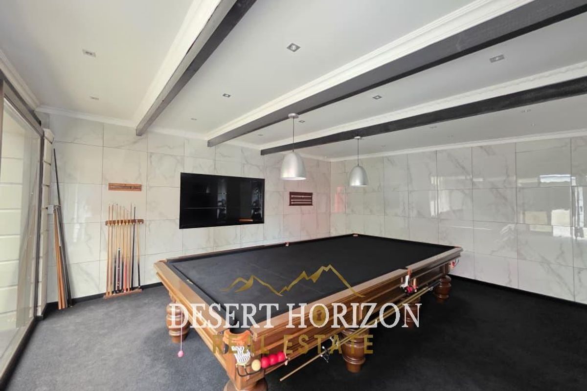Spacious entertainment room featuring marble-look wall tiles, decorative ceiling beams, recessed lighting, and large sliding glass doors.