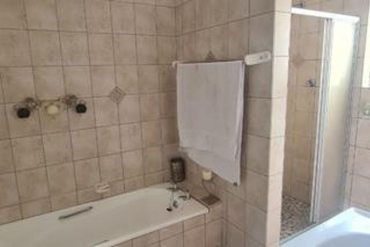 A functional bathroom featuring a built-in bathtub, separate shower enclosure with glass door, and neutral wall tiling throughout.