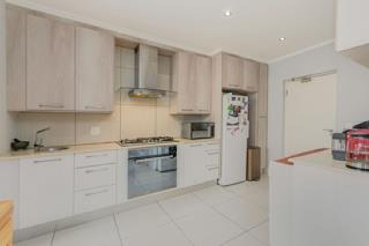 Modern kitchen featuring light wood-toned cabinetry, gas hob with extractor fan, built-in oven, and tiled flooring in a clean, functional layout.
