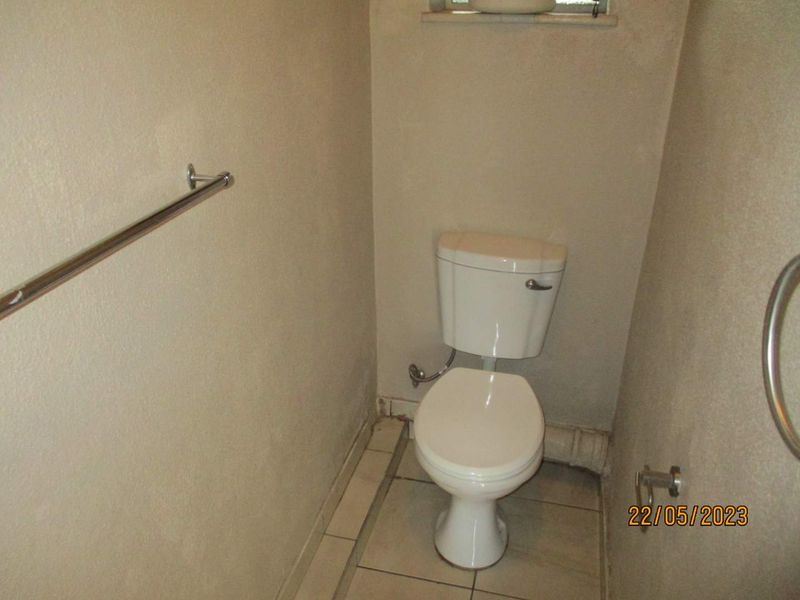 A compact bathroom featuring a standard toilet, tiled flooring, and wall-mounted grab and towel rails.