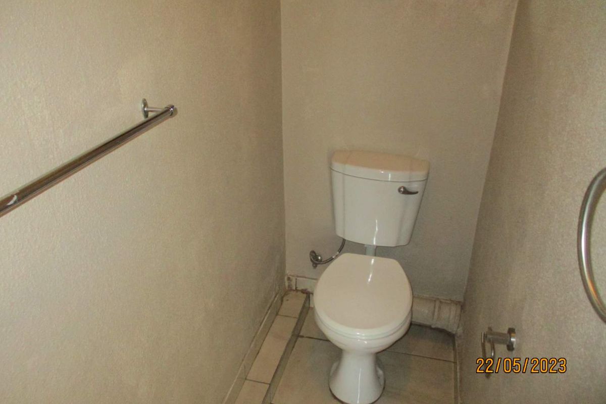 A compact bathroom featuring a standard toilet, tiled flooring, and wall-mounted grab and towel rails.