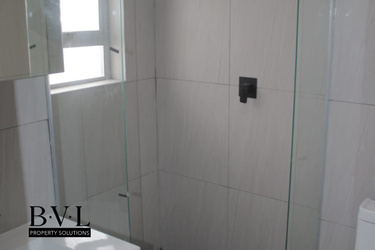 Modern bathroom featuring a glass-enclosed shower with matte black fixtures and neutral wall tiling.