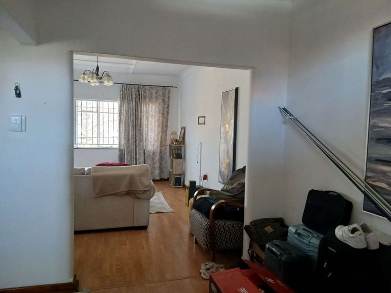 A view into a living room area featuring laminate flooring and a window with security bars, showing potential for updated finishes.