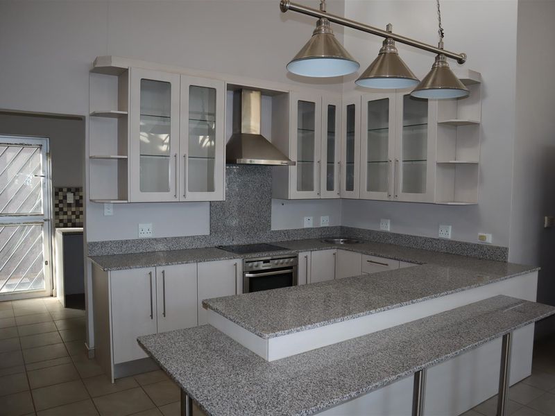 Modern kitchen featuring granite countertops, built-in oven, electric hob, stainless steel extractor fan, and glass-fronted cabinetry with a breakfast bar.