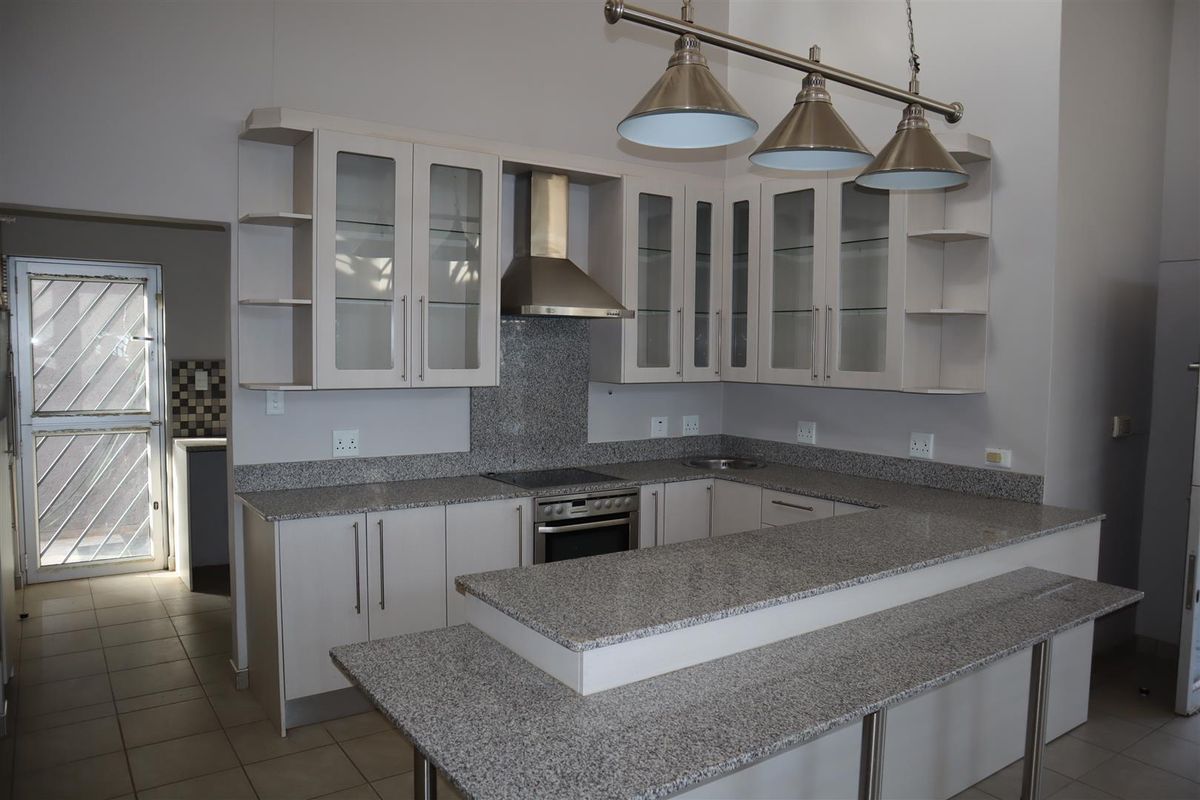 Modern kitchen featuring granite countertops, built-in oven, electric hob, stainless steel extractor fan, and glass-fronted cabinetry with a breakfast bar.