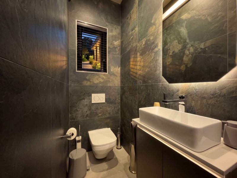 Modern guest bathroom featuring dark slate wall tiling, a sleek vessel sink on a vanity cabinet, and a wall-mounted toilet with concealed cistern.