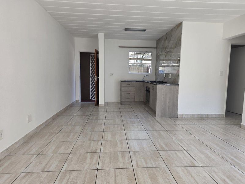 An open-plan living and kitchen area featuring tiled flooring, modern cabinetry, and a stone-look backsplash, providing a clean and functional space.