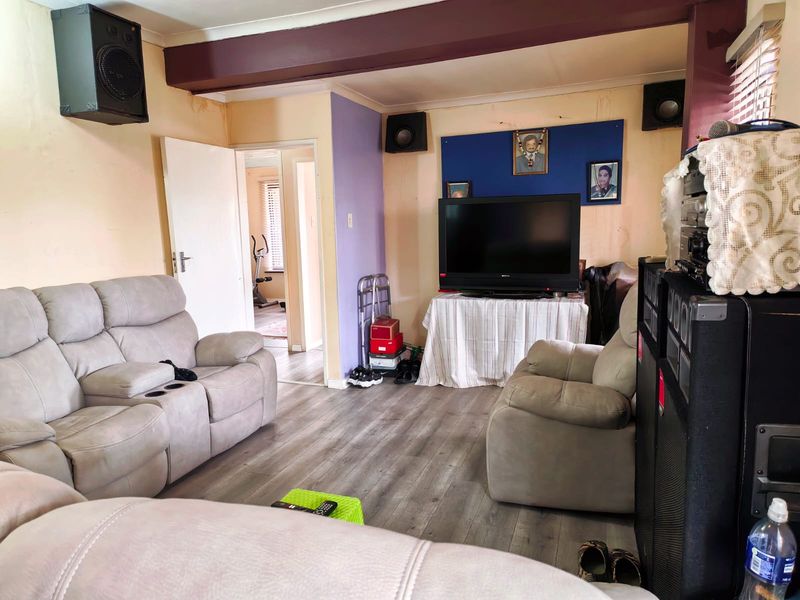 A living room featuring laminate flooring and an exposed ceiling beam, currently showing signs of wear including wall and ceiling damage.
