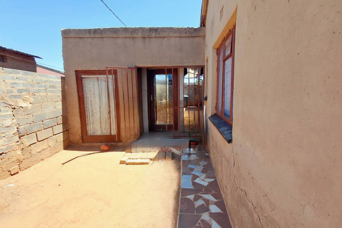 Rear exterior view of the property featuring a small courtyard, security gates, and a tiled walkway along the building facade.