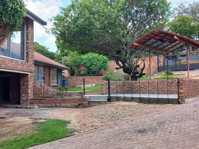 Rear exterior view of a face brick cottage featuring a paved driveway, retaining walls, and a covered outdoor patio area.