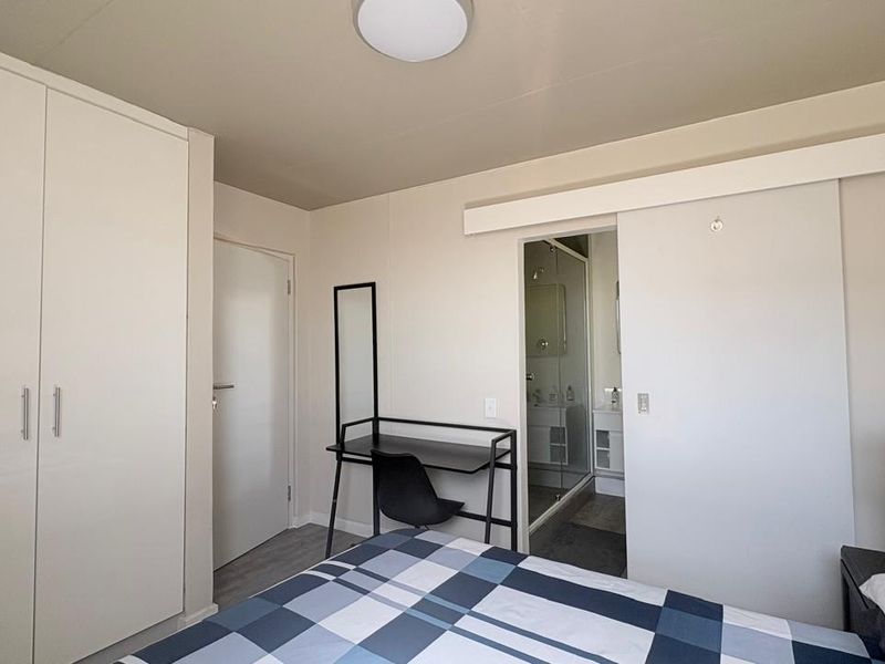 A well-maintained bedroom featuring a built-in wardrobe, sliding door access to an en-suite bathroom, and neutral finishes.