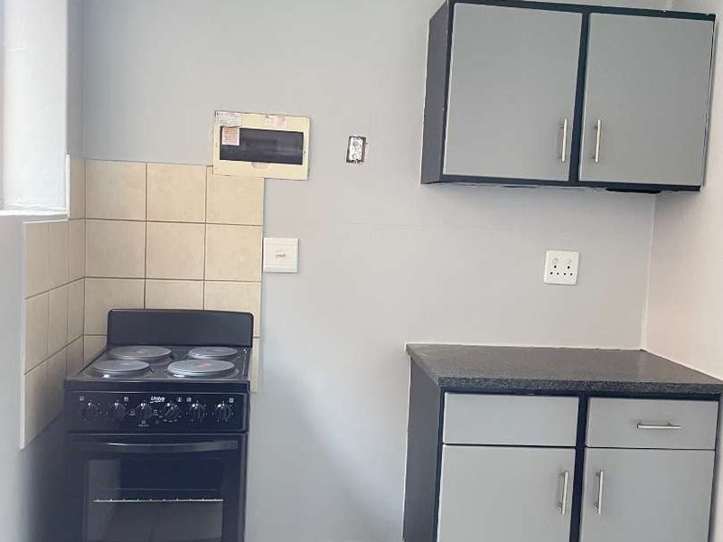 A compact kitchen area featuring basic cabinetry, a tiled splashback, and a freestanding stove, offering a functional space ready for updates.