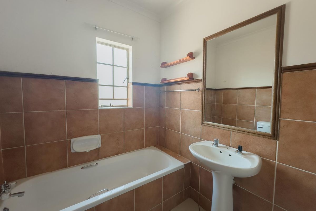 A functional bathroom featuring a pedestal basin, a standard bathtub with tiled surround, and a wall-mounted mirror.