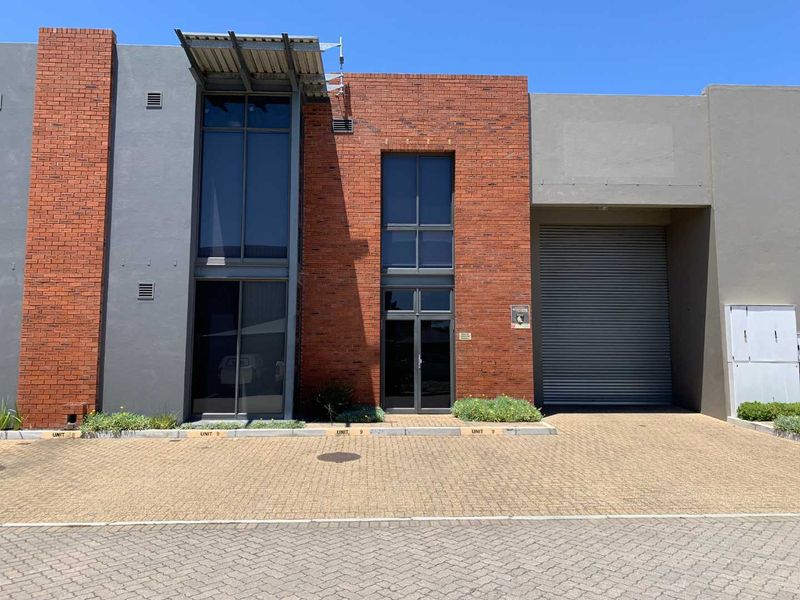 Modern industrial unit facade featuring a combination of face brick and rendered walls, large aluminium windows, and a secure roller shutter door.