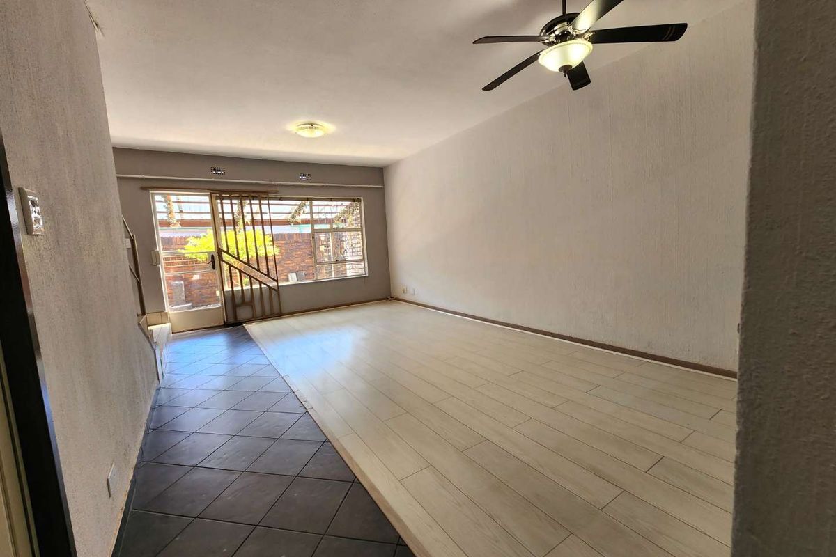 Spacious living area featuring a combination of tiled and wood-look flooring, a ceiling fan, and large windows providing natural light.