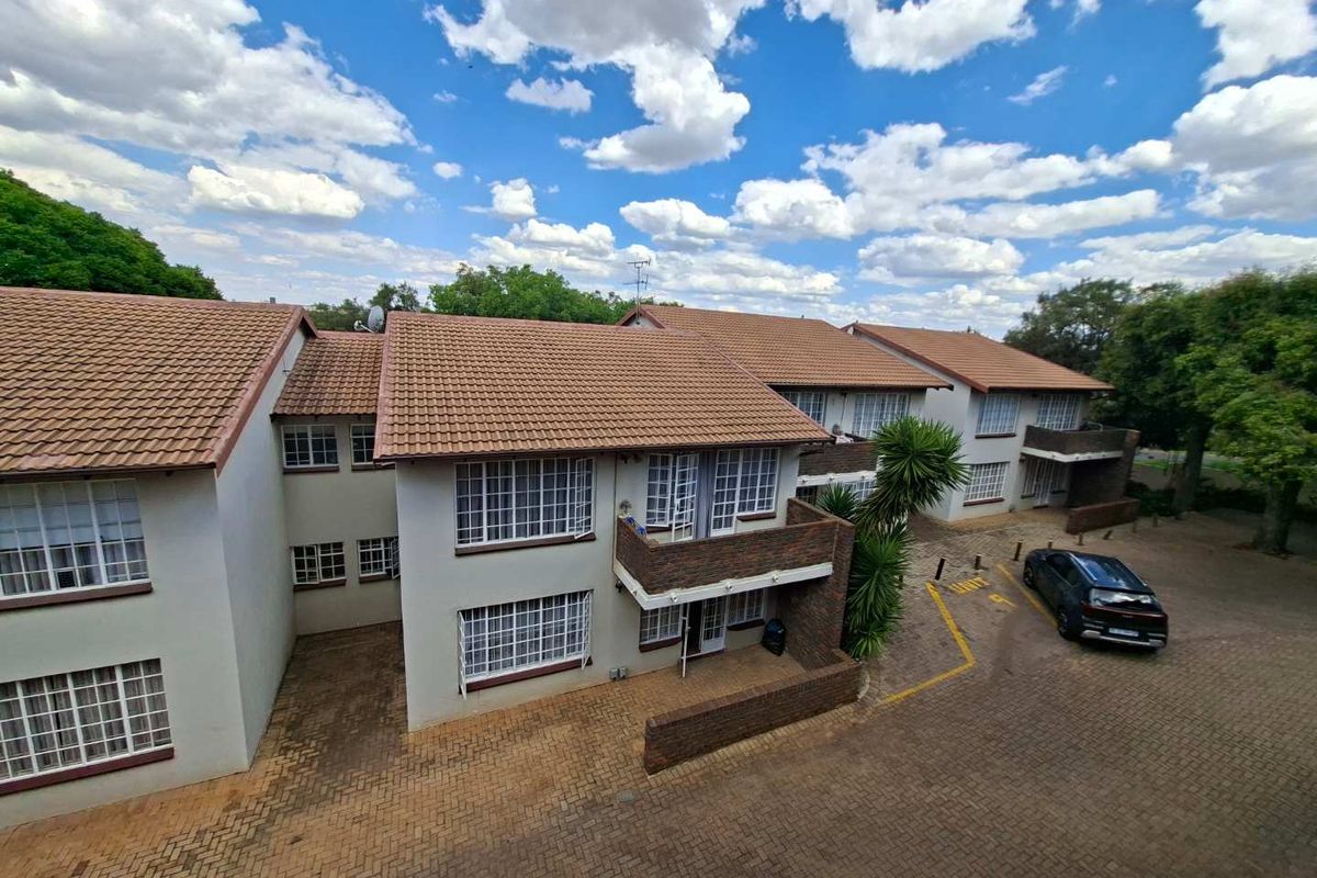 An elevated aerial view of a residential apartment complex featuring tiled roofs, brick facades, and paved driveway areas.