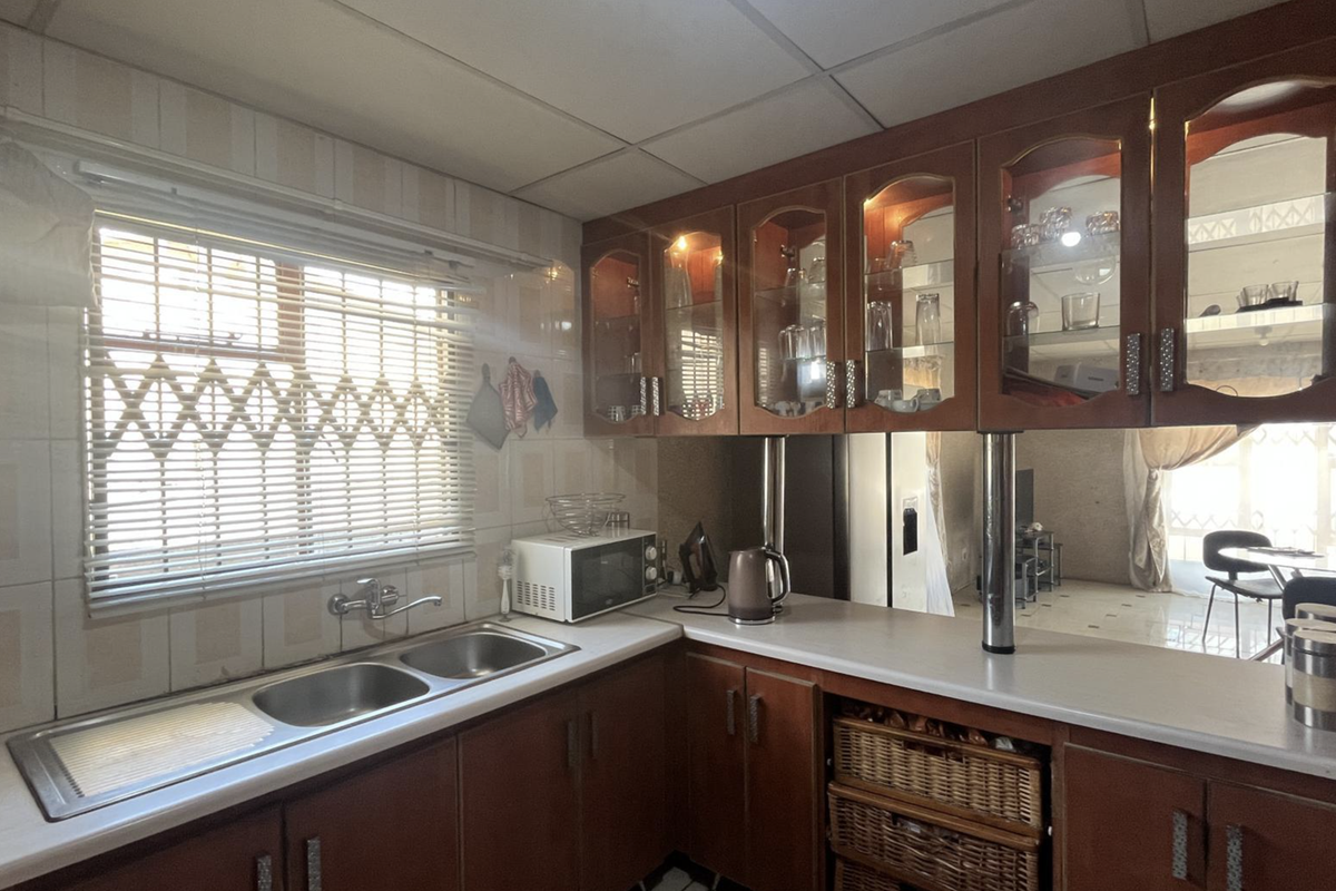 A functional kitchen featuring wooden cabinetry, double bowl sink, and tiled splashbacks, offering a classic layout with potential for modern updates.