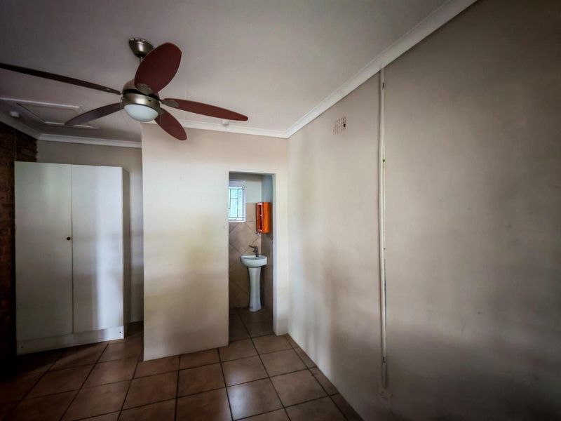 A bedroom featuring tiled flooring, a ceiling fan, and a built-in cupboard, with an adjoining small en-suite area containing a pedestal basin.