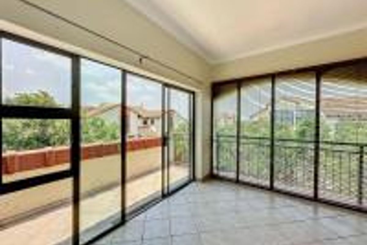 Bright and spacious living area featuring large sliding glass doors that open onto a balcony, finished with neutral floor tiles and cove cornicing.