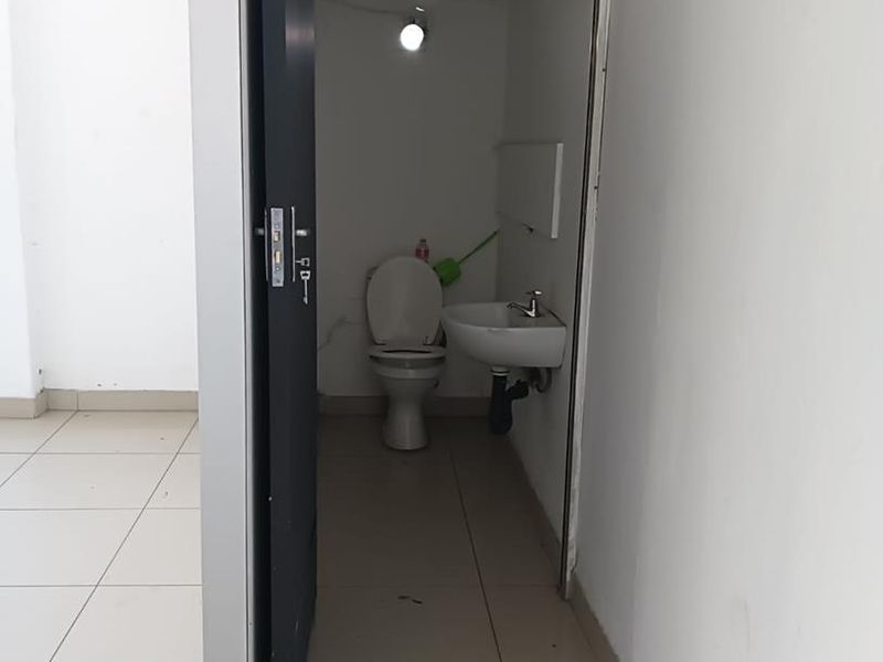 A small, functional bathroom featuring a standard toilet and wall-mounted basin, accessible from the main tiled living area.