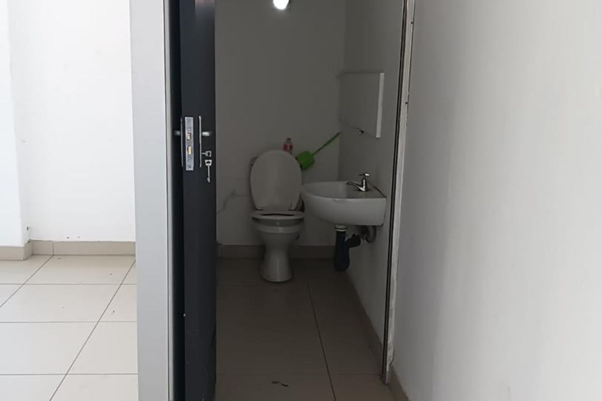 A small, functional bathroom featuring a standard toilet and wall-mounted basin, accessible from the main tiled living area.