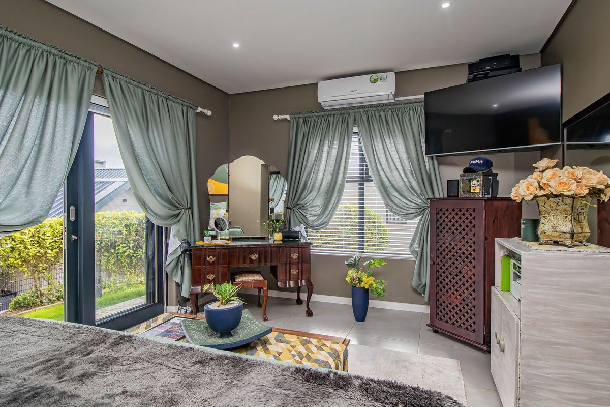 A well-maintained bedroom featuring tiled flooring, recessed ceiling lighting, a wall-mounted air conditioning unit, and sliding glass doors providing access to the garden.