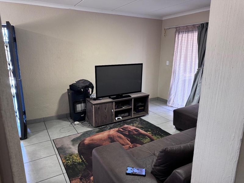 A functional living room area featuring tiled flooring and access to an outdoor space through a sliding door with a security gate.