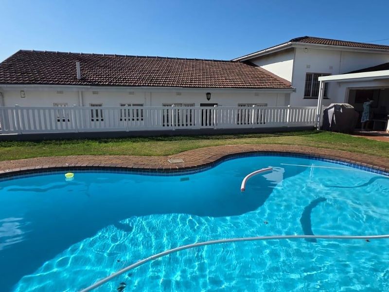 A well-maintained swimming pool area featuring brick coping, a white perimeter fence, and an adjacent covered patio area.