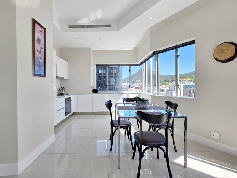 Modern open-plan kitchen and dining area featuring sleek white cabinetry, integrated appliances, polished tile floors, and expansive windows with mountain and city views.
