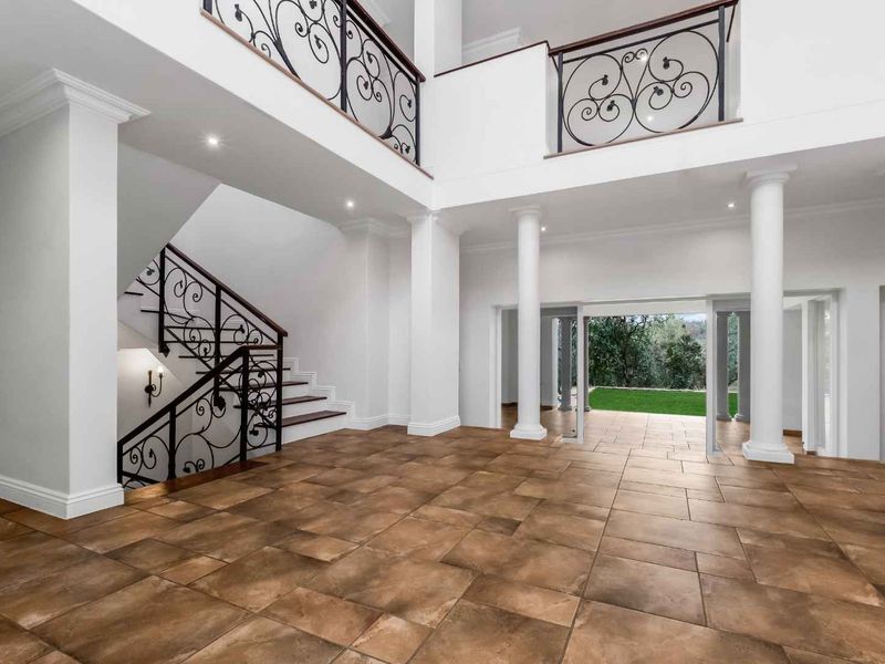 Spacious grand entrance hall featuring tiled flooring, a striking wrought iron staircase, and an open-plan design leading to the rear garden.