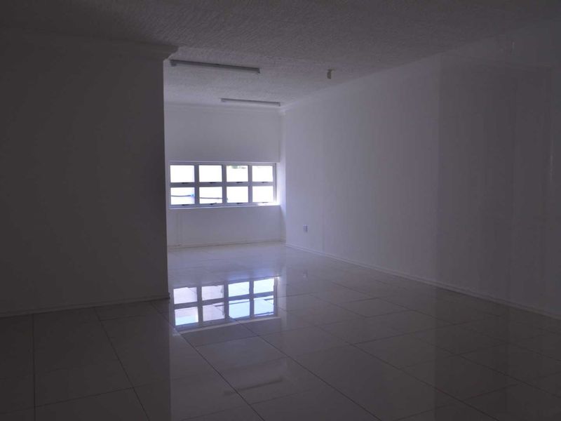 An empty, open-plan living area featuring polished tiled flooring, neutral walls, and natural light from a multi-pane window.