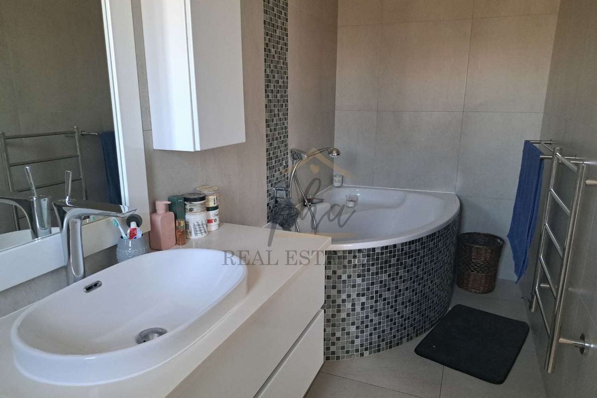 Modern bathroom featuring a corner bathtub with mosaic tile surround, a sleek vanity with a vessel sink, and a wall-mounted heated towel rail.