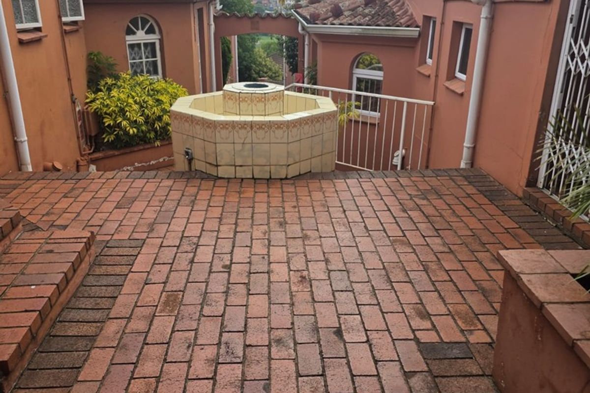 Rear courtyard area featuring brick paving, a central tiled fountain, and surrounding townhouse architecture with terracotta roof tiles.