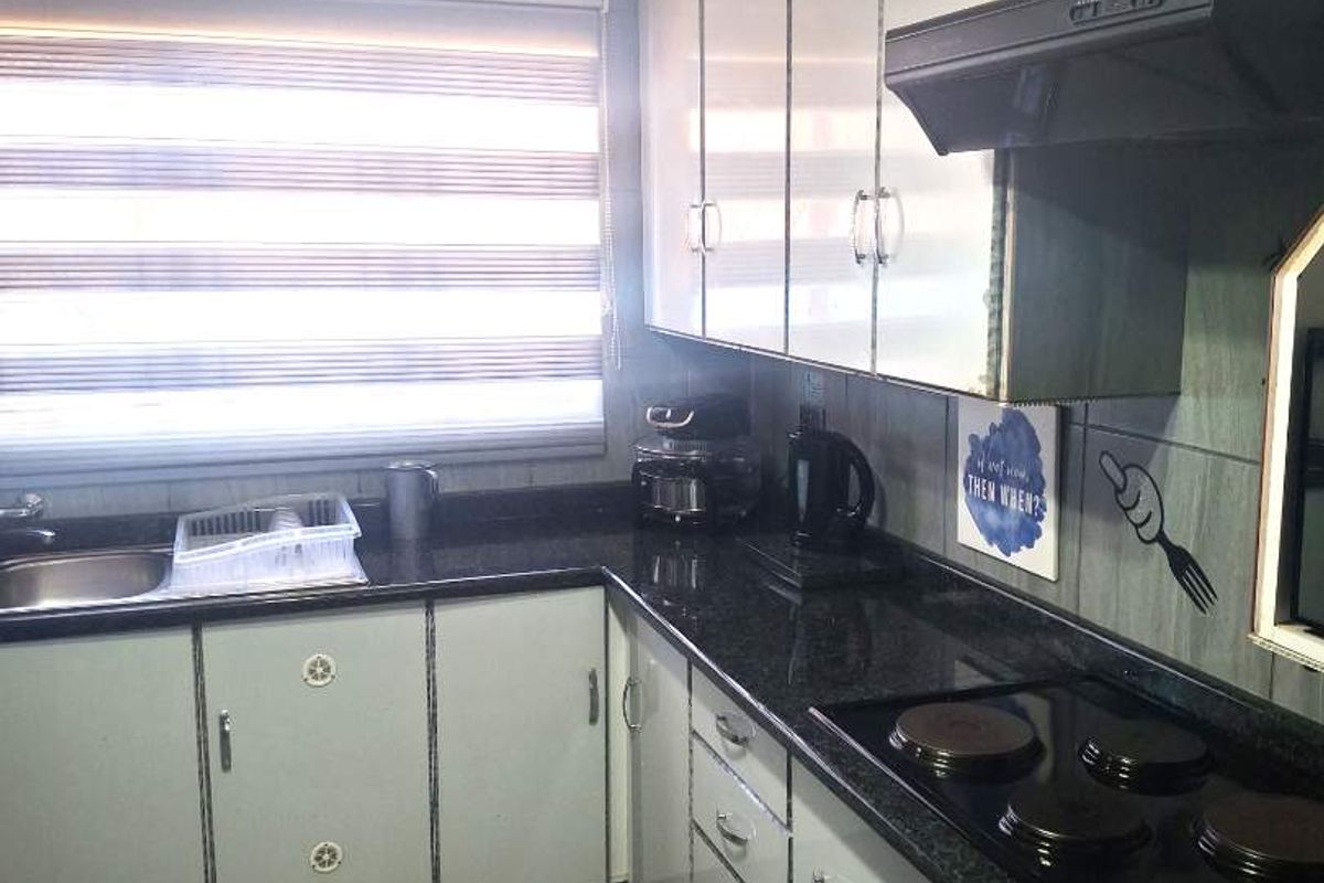 A functional kitchen featuring dark granite countertops, white cabinetry, a built-in electric hob, and an extractor fan with tiled flooring.