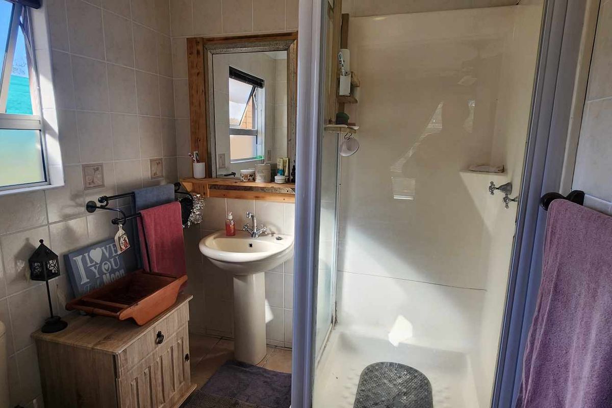 A functional bathroom featuring a pedestal basin, a glass-enclosed shower, and a toilet, finished with neutral wall tiling and natural light.