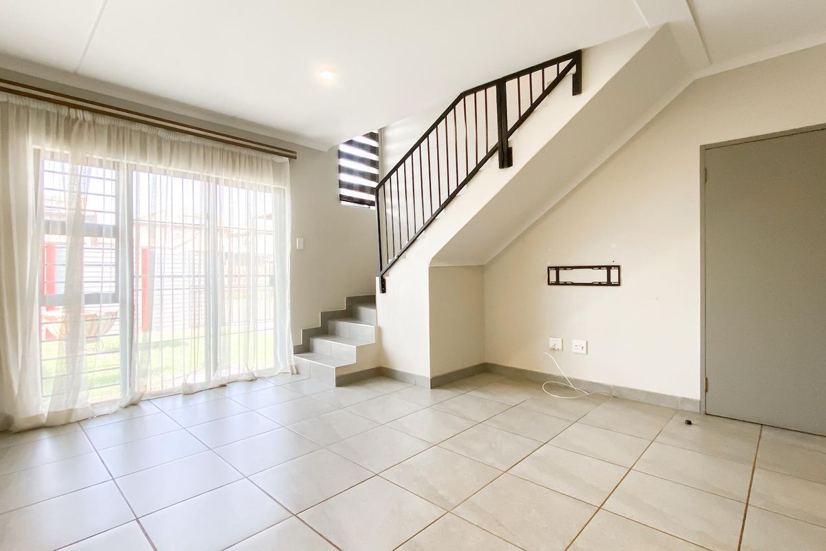 A bright, open-plan living area featuring neutral tiled flooring, a modern staircase with a metal balustrade, and large sliding doors leading outdoors.