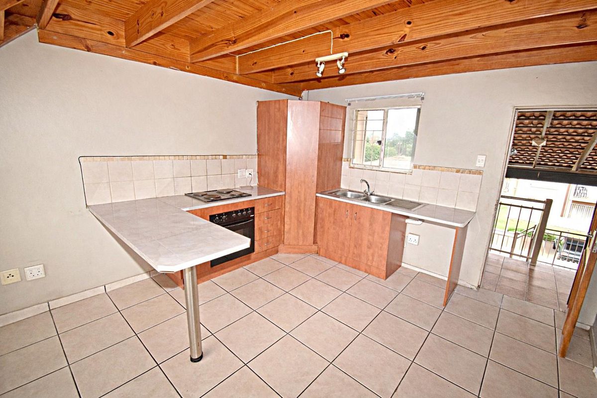 A functional kitchen featuring tiled flooring, built-in cabinetry, a stove with oven, and a double sink, set under exposed timber ceiling beams.