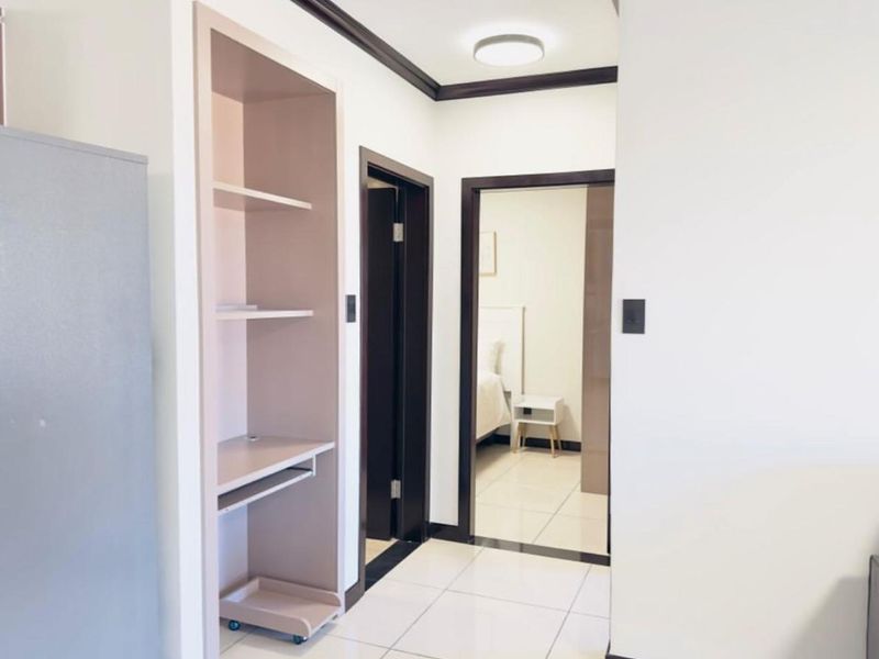 A clean and well-maintained hallway featuring tiled flooring, dark wood trim, and a built-in shelving unit, providing access to adjacent rooms.