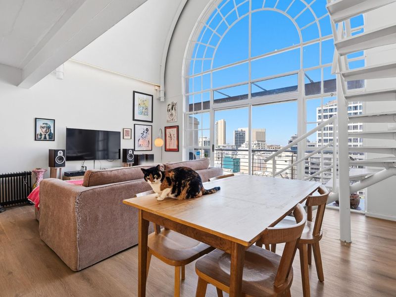 Spacious open-plan living area featuring a striking arched window, vaulted ceilings, and a modern spiral staircase leading to an upper level.