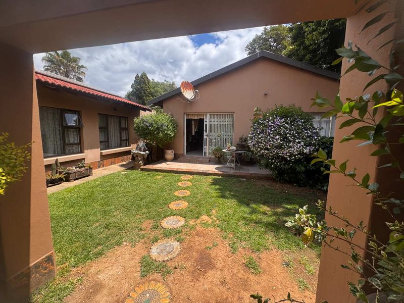 A view of the rear garden and patio area, featuring a lawn, paved pathway, and access to the home via a sliding glass door.