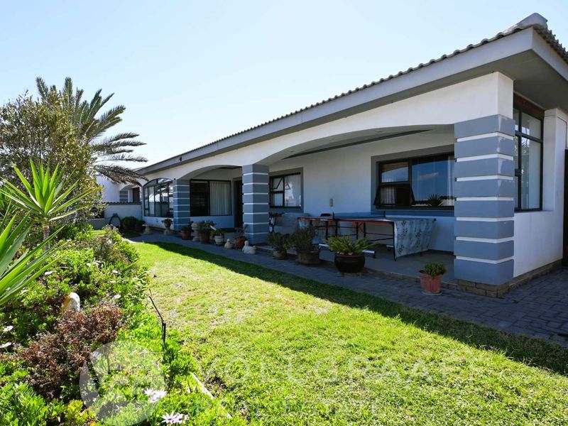 A well-maintained rear exterior view featuring a covered patio with brick pillars, overlooking a neat lawn and landscaped garden area.