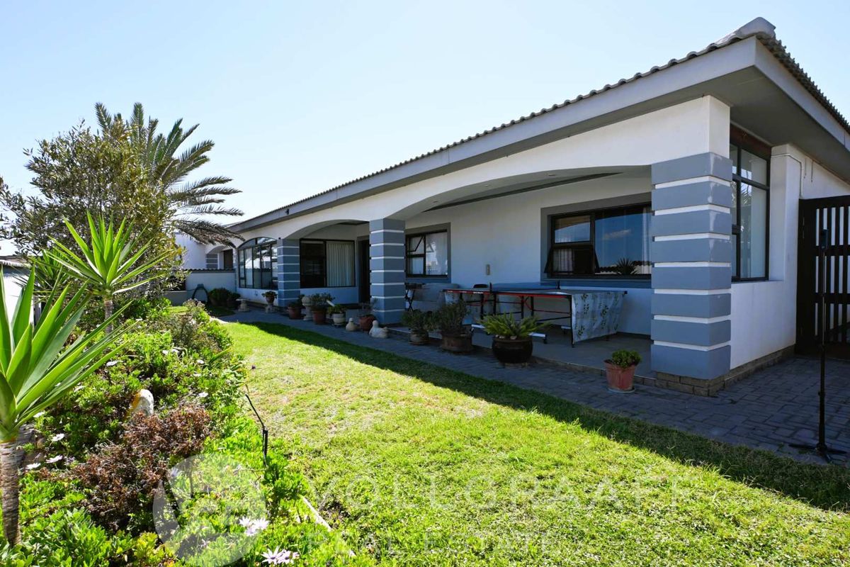 A well-maintained rear exterior view featuring a covered patio with brick pillars, overlooking a neat lawn and landscaped garden area.
