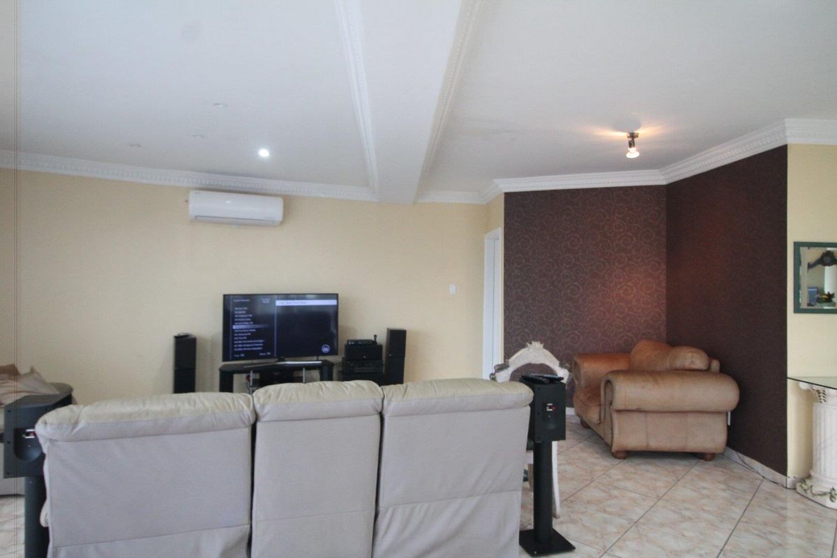 A spacious living room featuring tiled flooring, decorative ceiling cornices, and a wall-mounted air conditioning unit.