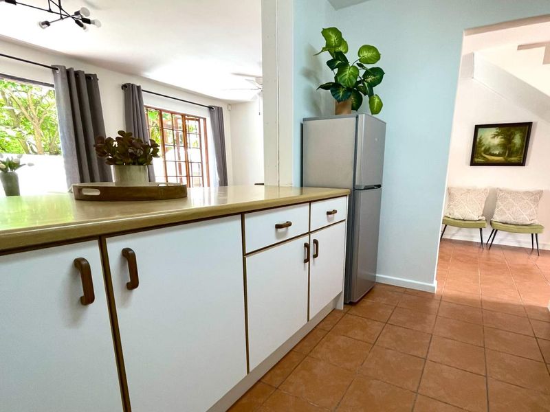 A functional kitchen area featuring white cabinetry, laminate countertops, and ceramic tile flooring, with an open-plan layout connecting to the adjacent living space.