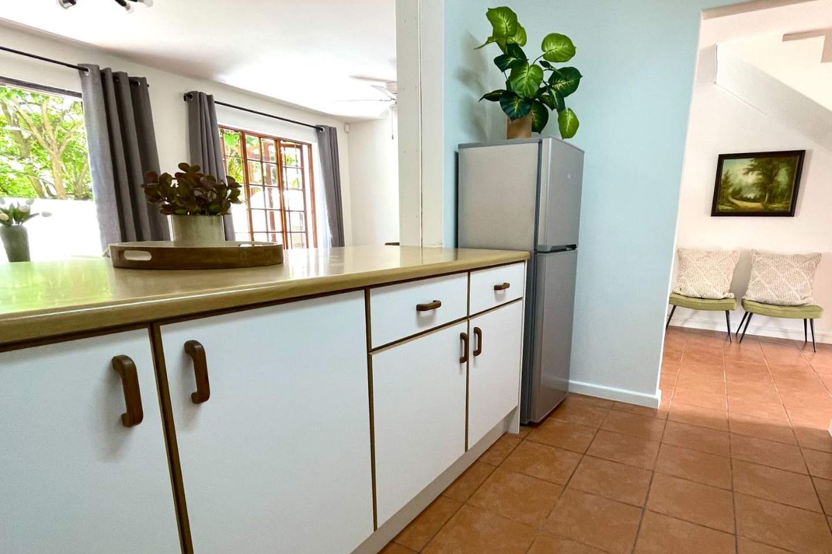 A functional kitchen area featuring white cabinetry, laminate countertops, and ceramic tile flooring, with an open-plan layout connecting to the adjacent living space.