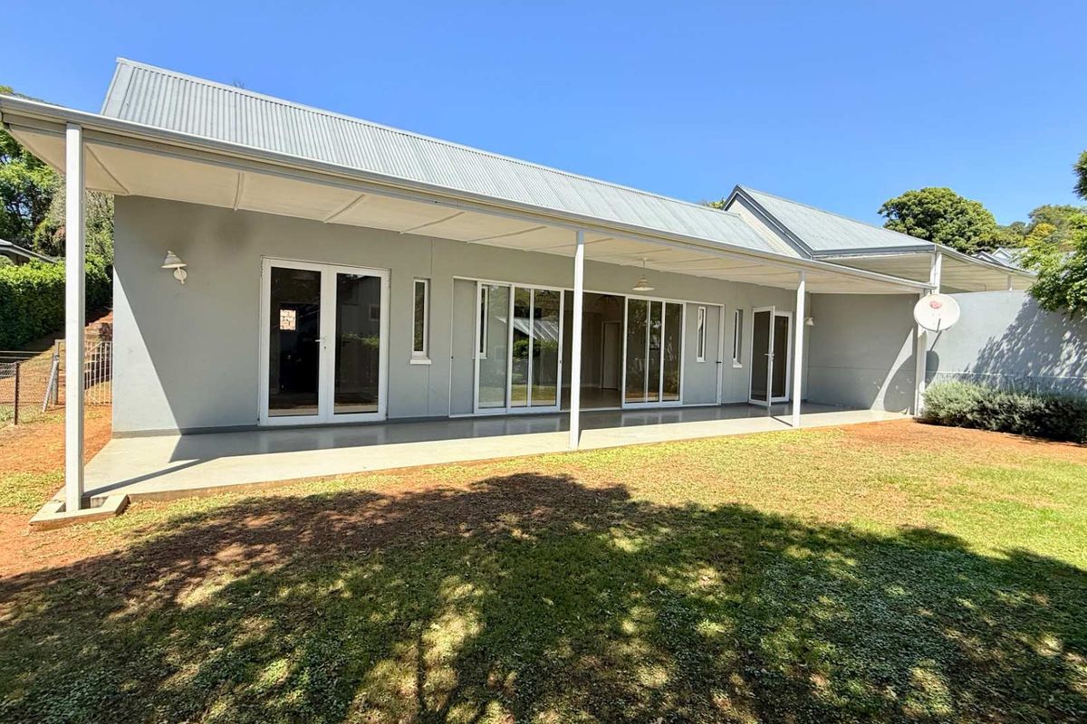 Rear view of the townhouse featuring a spacious covered patio, multiple glass access points, and a well-maintained garden area.