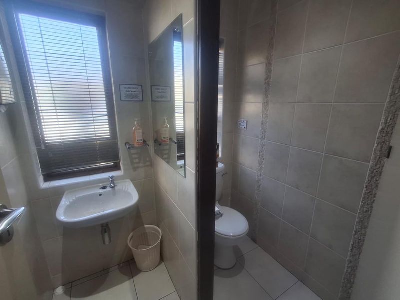 A functional bathroom featuring a wall-mounted basin, toilet, and neutral ceramic tiling throughout, providing a clean and practical space.