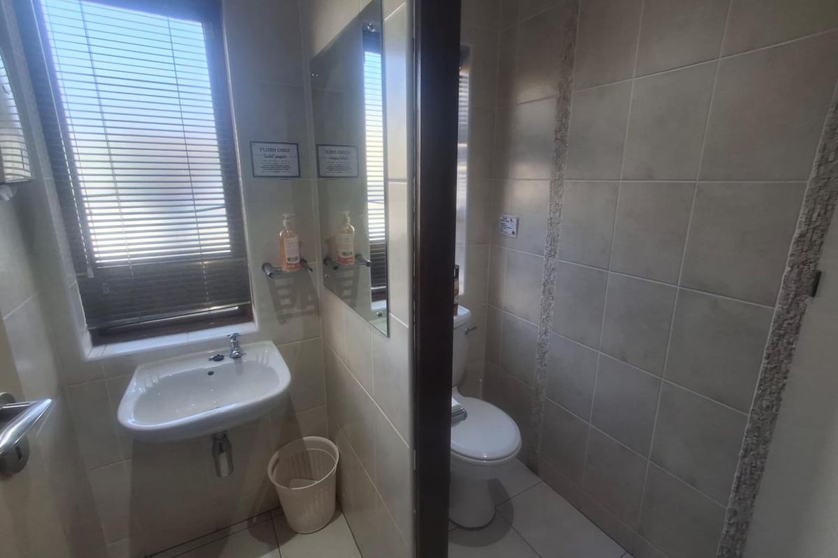 A functional bathroom featuring a wall-mounted basin, toilet, and neutral ceramic tiling throughout, providing a clean and practical space.