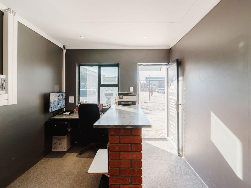A functional office space featuring a brick-based service counter, carpeted flooring, and direct access to the exterior through a glass-panelled door.